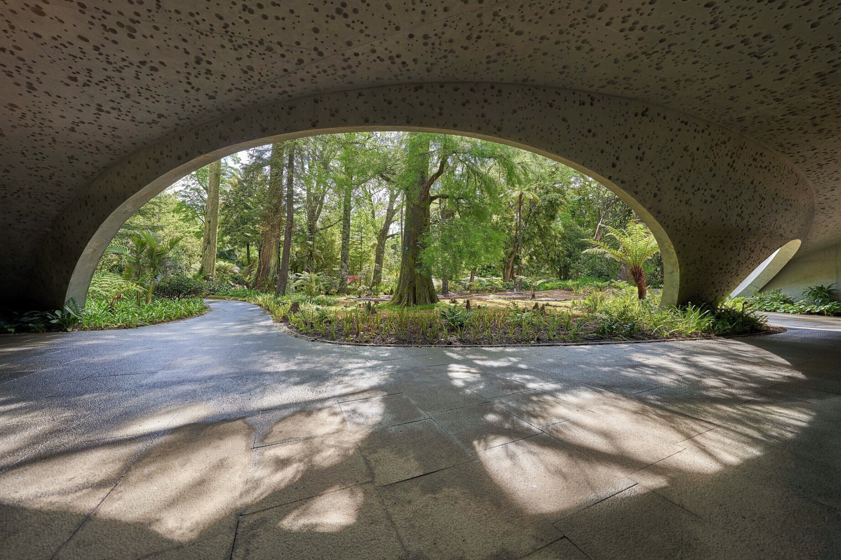 A covered pathway with a view of a forested area through a large archway.