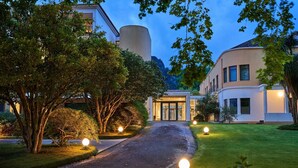 A pathway leading to a building with a glass entrance, surrounded by trees and illuminated by ground lights. - Terra Nostra Garden Hotel (Povoacao)