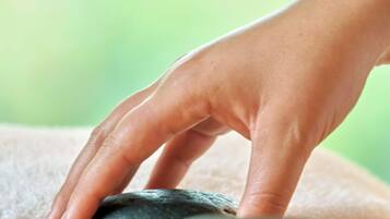 A hand resting on smooth, dark stones, likely used for a massage or relaxation technique.
