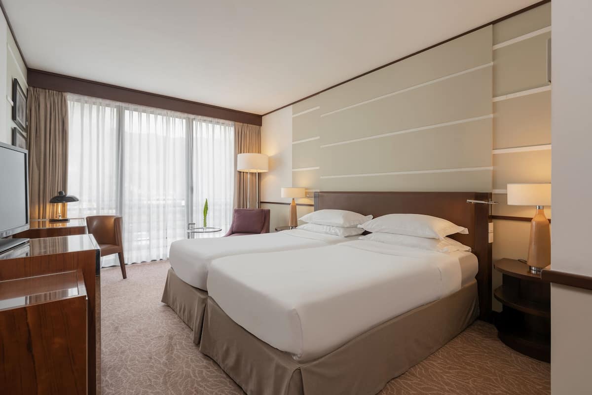 A hotel room with two beds, a desk, a chair, a TV, and a lamp.