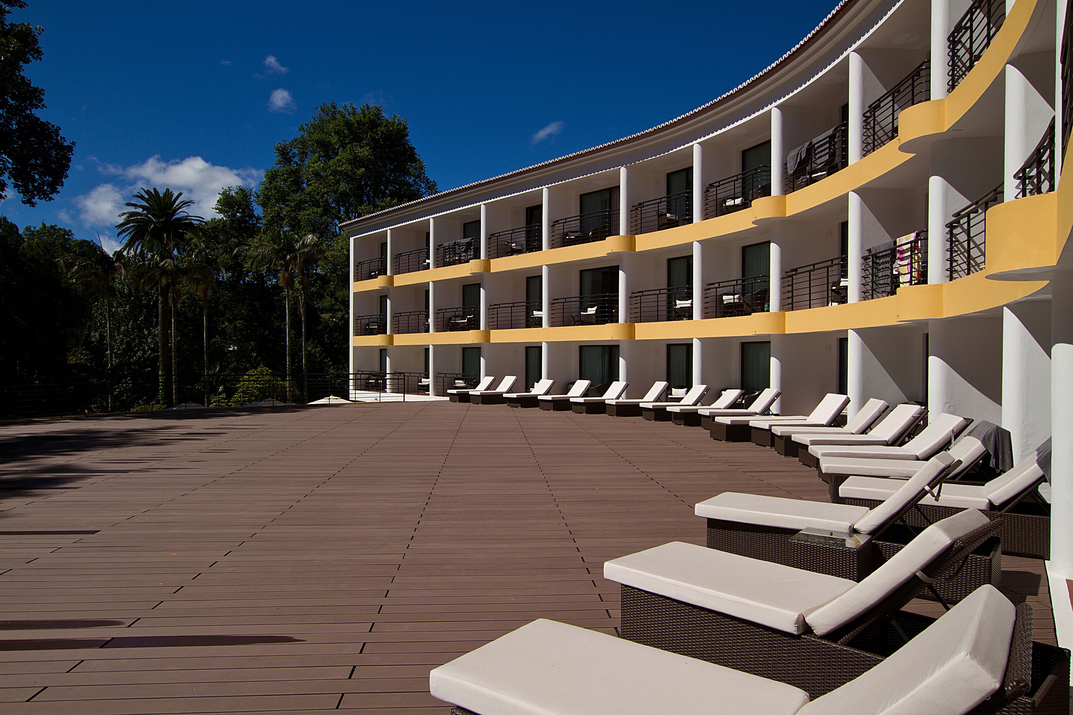 Un hotel de varios pisos con un balcón curvo, filas de tumbonas y una terraza de madera.