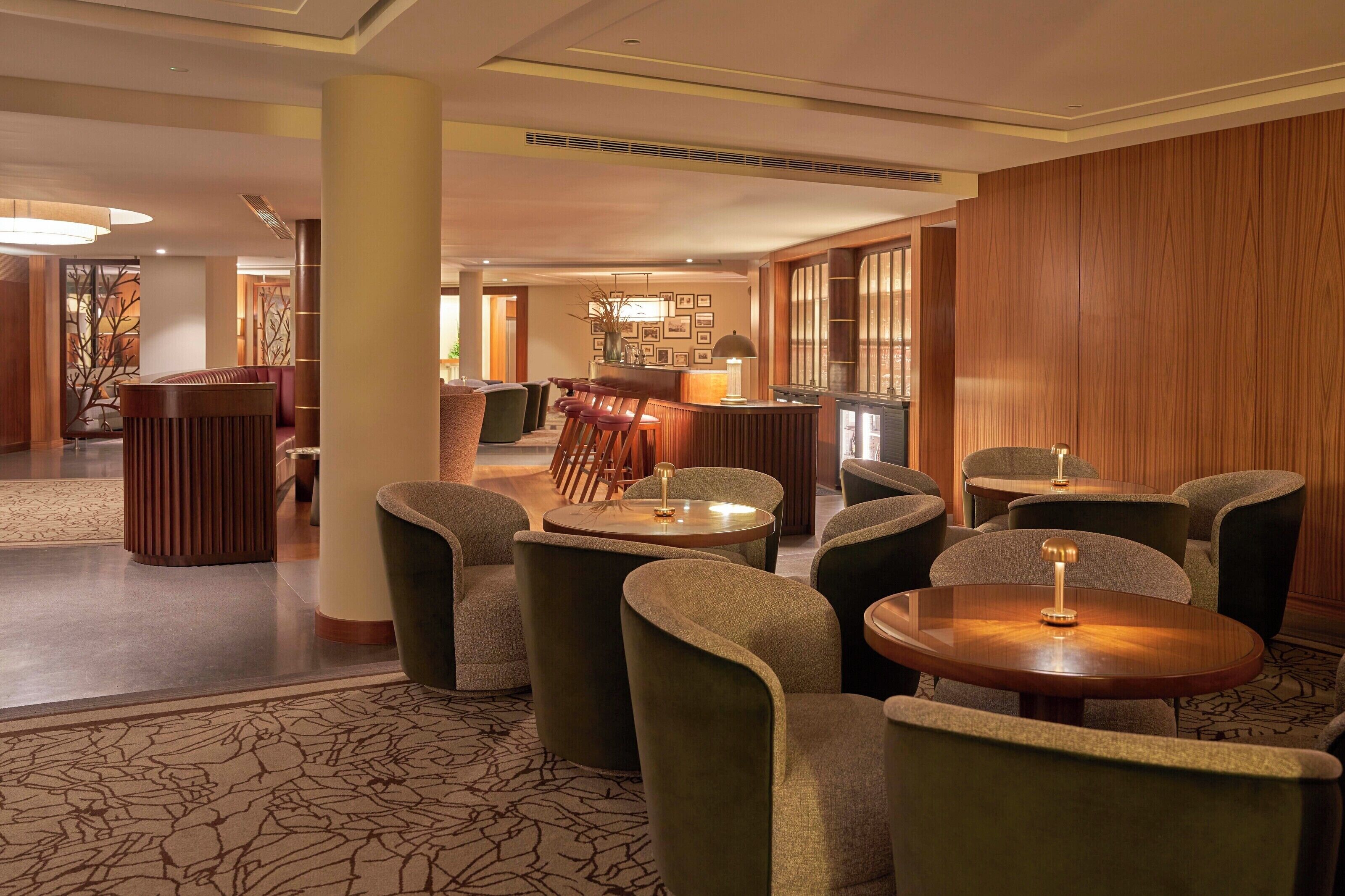 A hotel lobby with round tables and chairs, a reception desk, and a wooden wall.