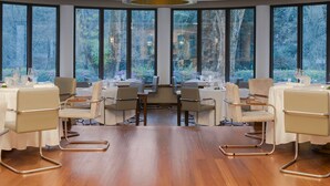 A modern dining area with round tables and chairs, large windows with a view of trees, and a circular light fixture on the ceiling. - Terra Nostra Garden Hotel (Povoacao)