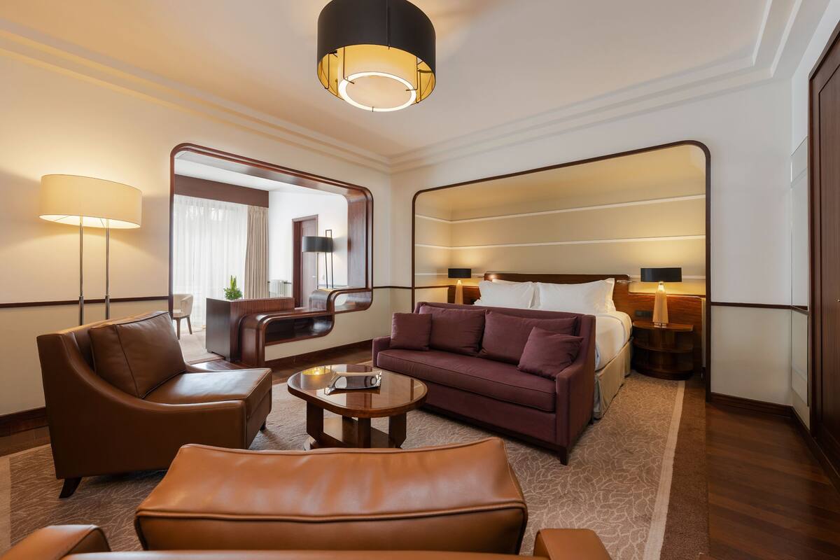 A modern hotel room with a large bed, a brown leather sofa, a small round table, and a large mirror.