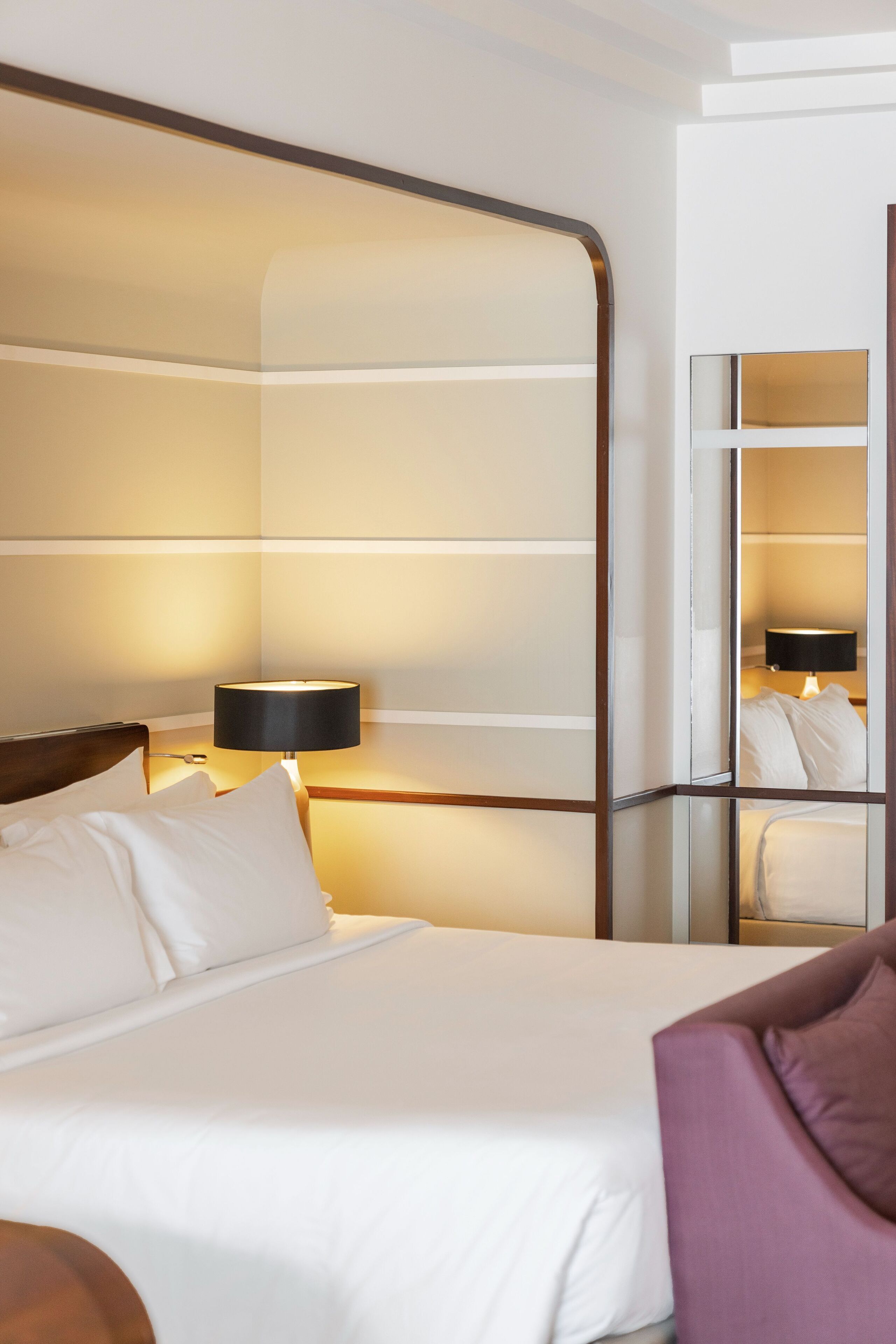 A hotel room with a bed, a nightstand, a lamp, and a mirror.