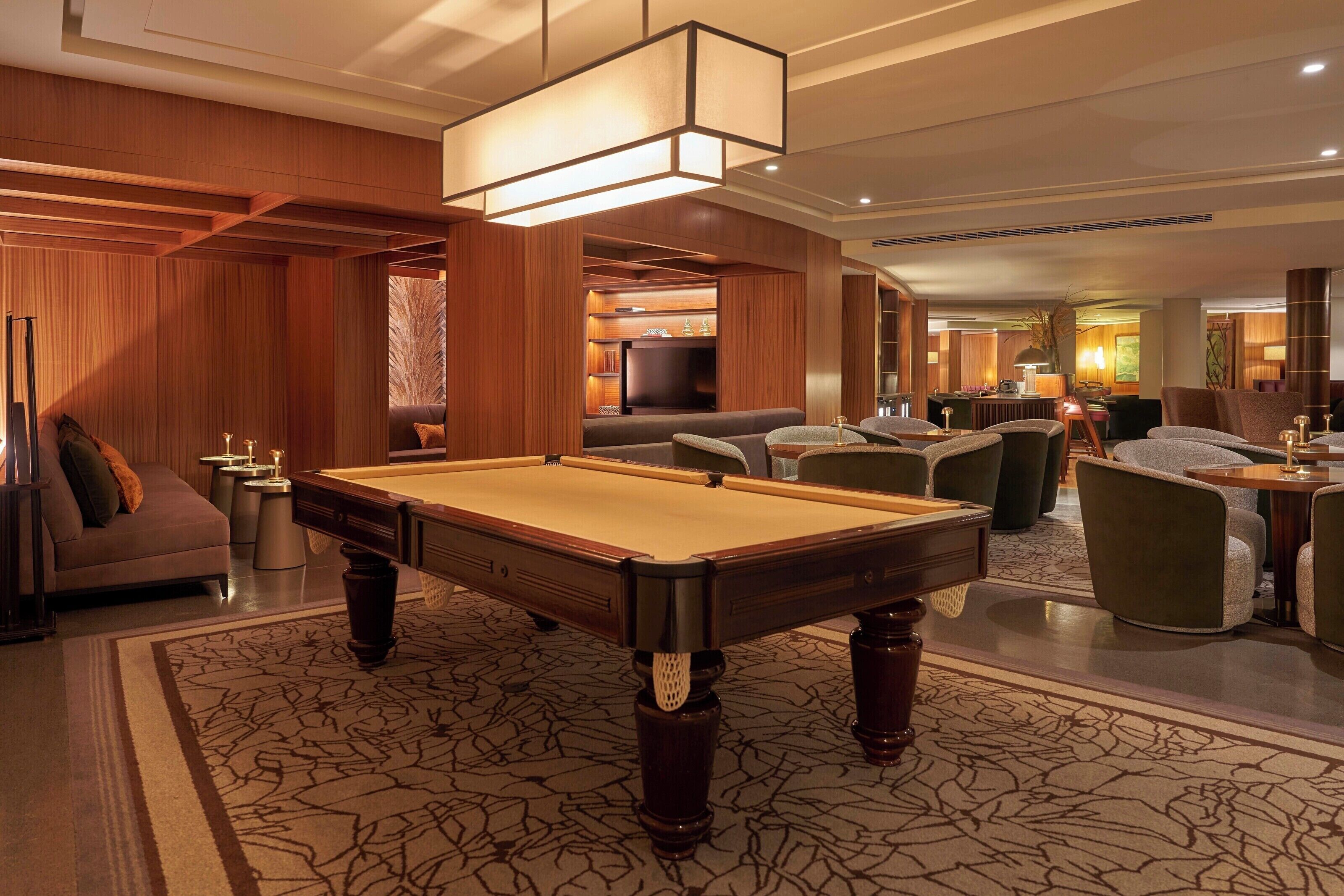 A pool table in a well-lit room with wooden paneling and a patterned carpet.