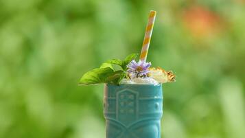 A blue glass with a straw, mint leaves, and purple flowers on a reflective surface.