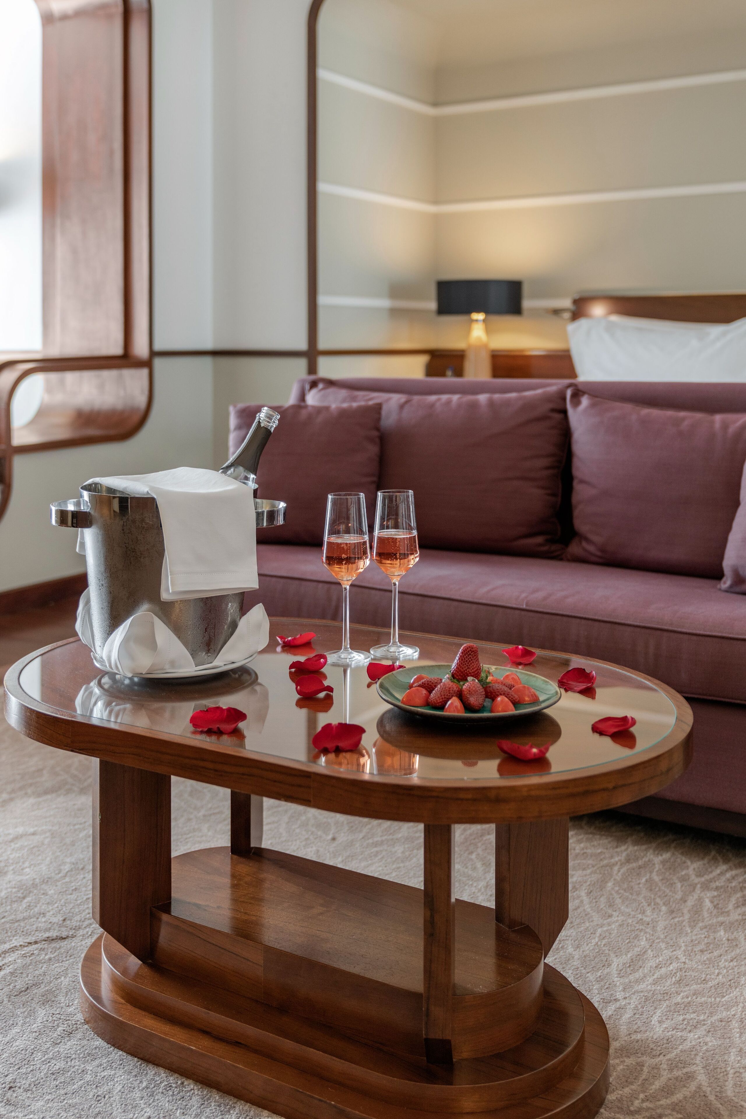 A cozy room with a wooden coffee table, a champagne bucket, two glasses of champagne, and a plate of strawberries.