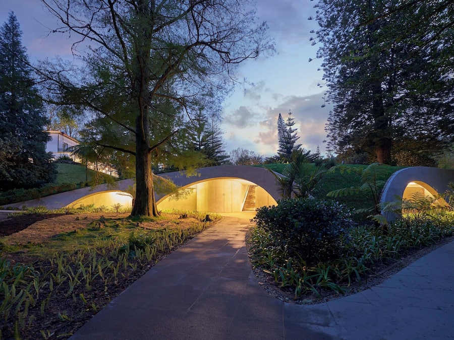A pathway leading to a modern, arched structure surrounded by lush greenery.