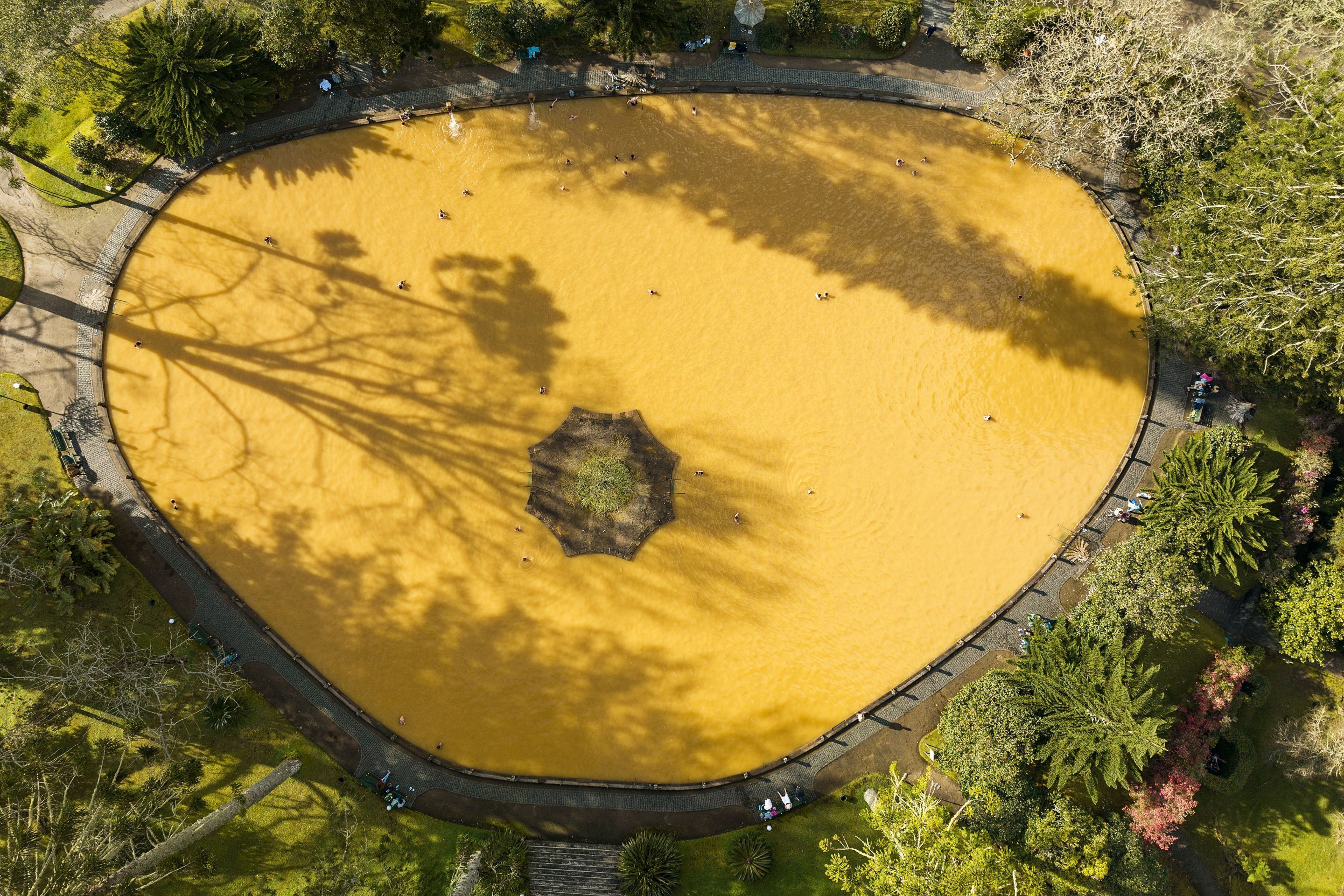 Vista aérea de un parque circular con una masa de agua amarillenta, rodeado de árboles y un sendero para caminar.