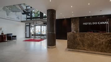 A modern hotel lobby with a reception desk, a large pillar, and a map on the wall.