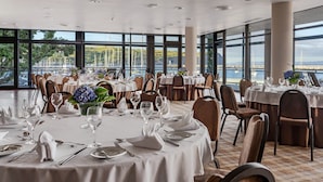 A restaurant with round tables set for dining, large windows offering a view of the sea and boats. - Hotel do Canal (Horta)