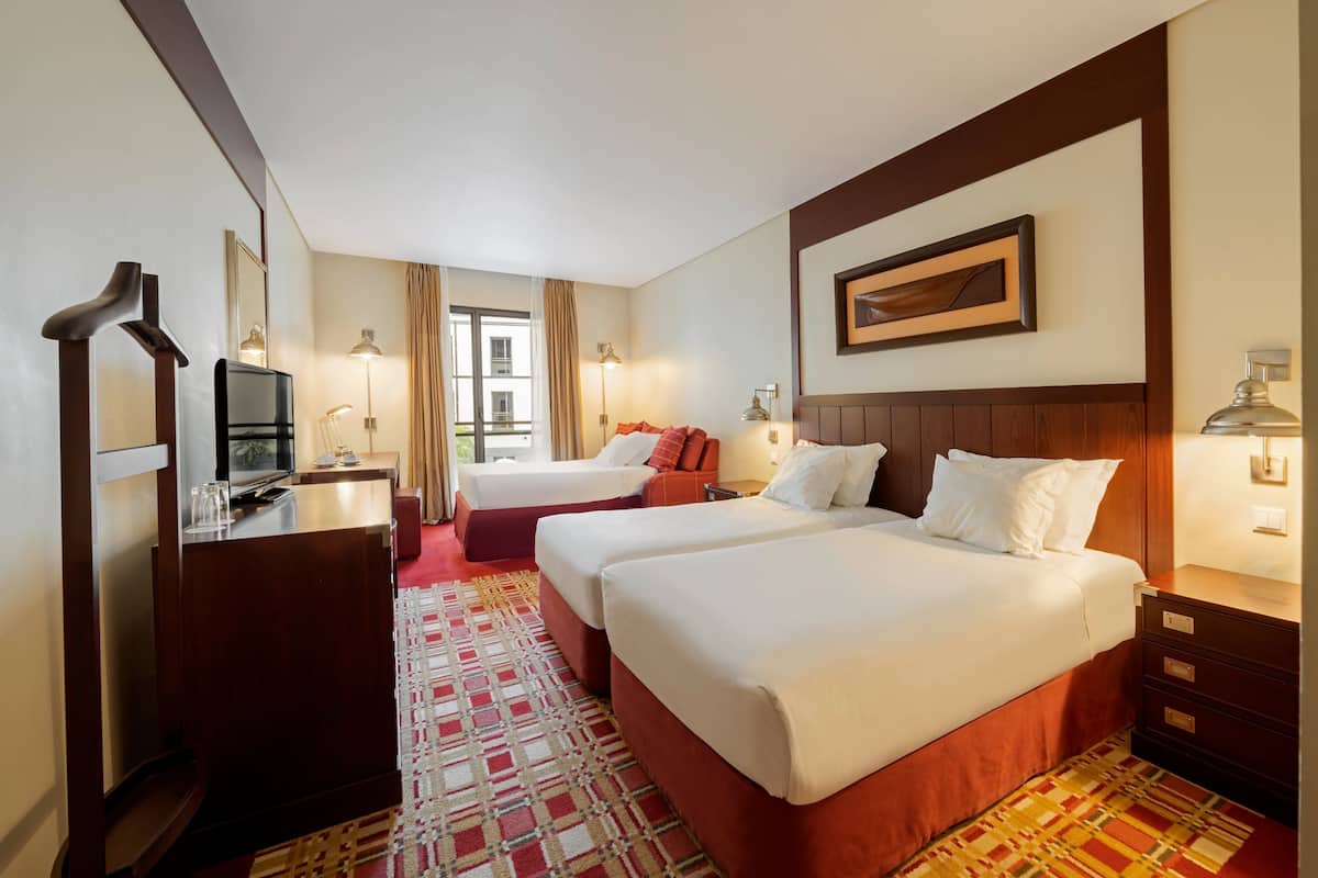 A hotel room with two beds, a desk with a TV, and a view of the outside.