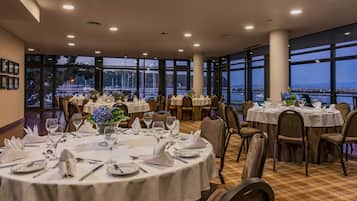 A restaurant with round tables set for dining, large windows offering a view of the water, and a checkered floor.