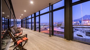 A spacious balcony with wooden flooring and large windows offering views of a marina and boats. - Hotel do Canal (Horta)