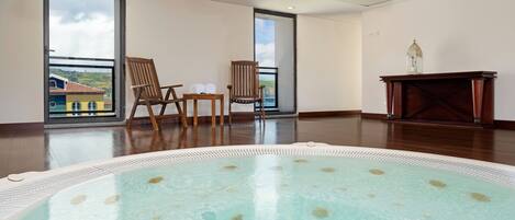 Una piscina interior espaciosa con agua cristalina, sillas de madera, una mesita y un armario de madera.