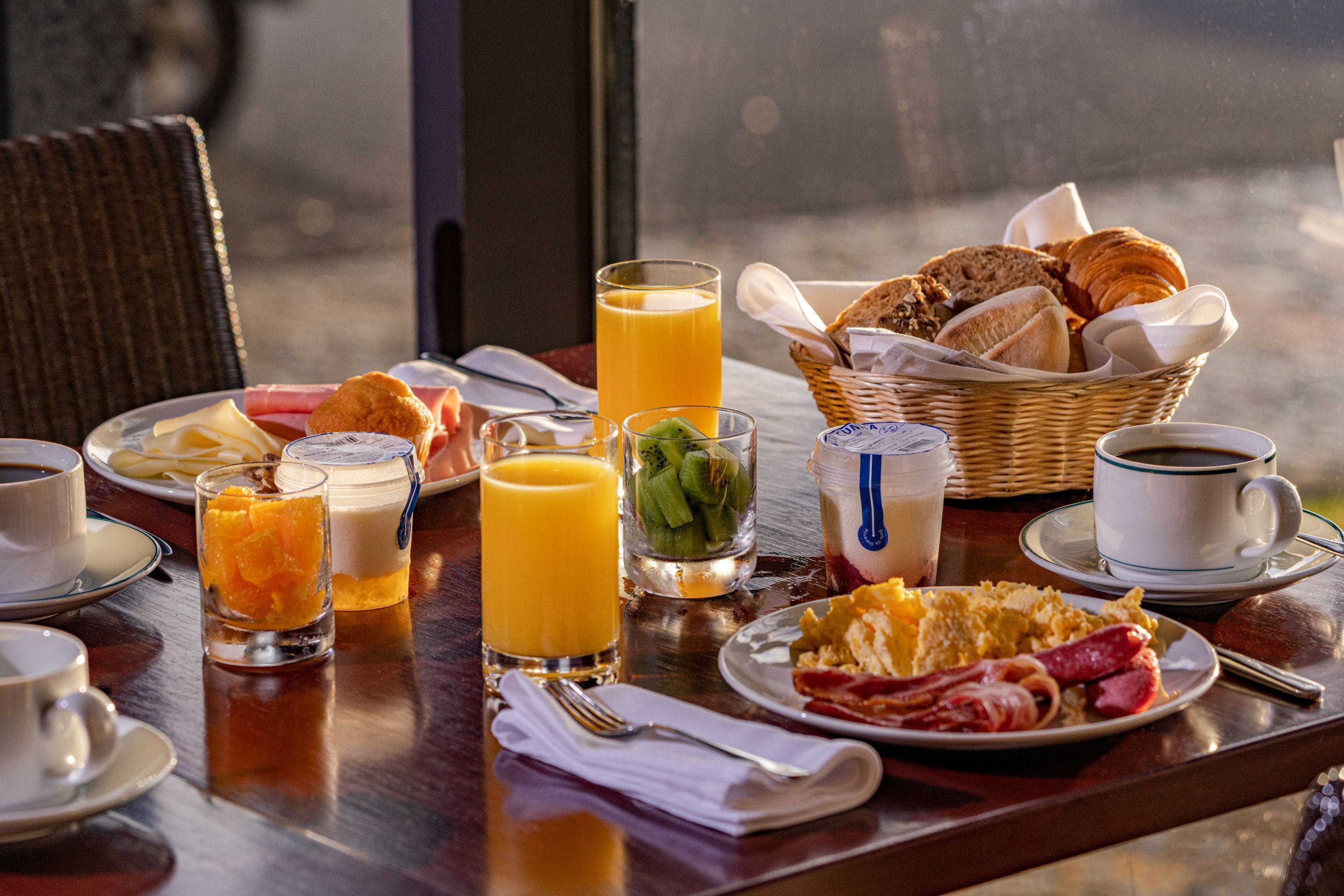Une table de petit-déjeuner avec des croissants, des œufs, du bacon et du jus de fruits.