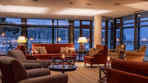 A spacious lounge area with a large window view of a marina, furnished with red sofas and armchairs, and a central coffee table. - Hotel do Canal (Horta)