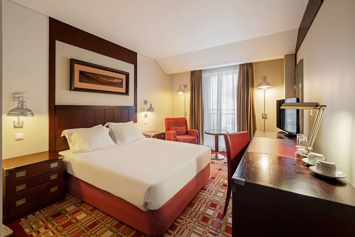 Ein Hotelzimmer mit Bett, Schreibtisch, Stuhl, Fernseher und einem fenster mit Vorhängen.