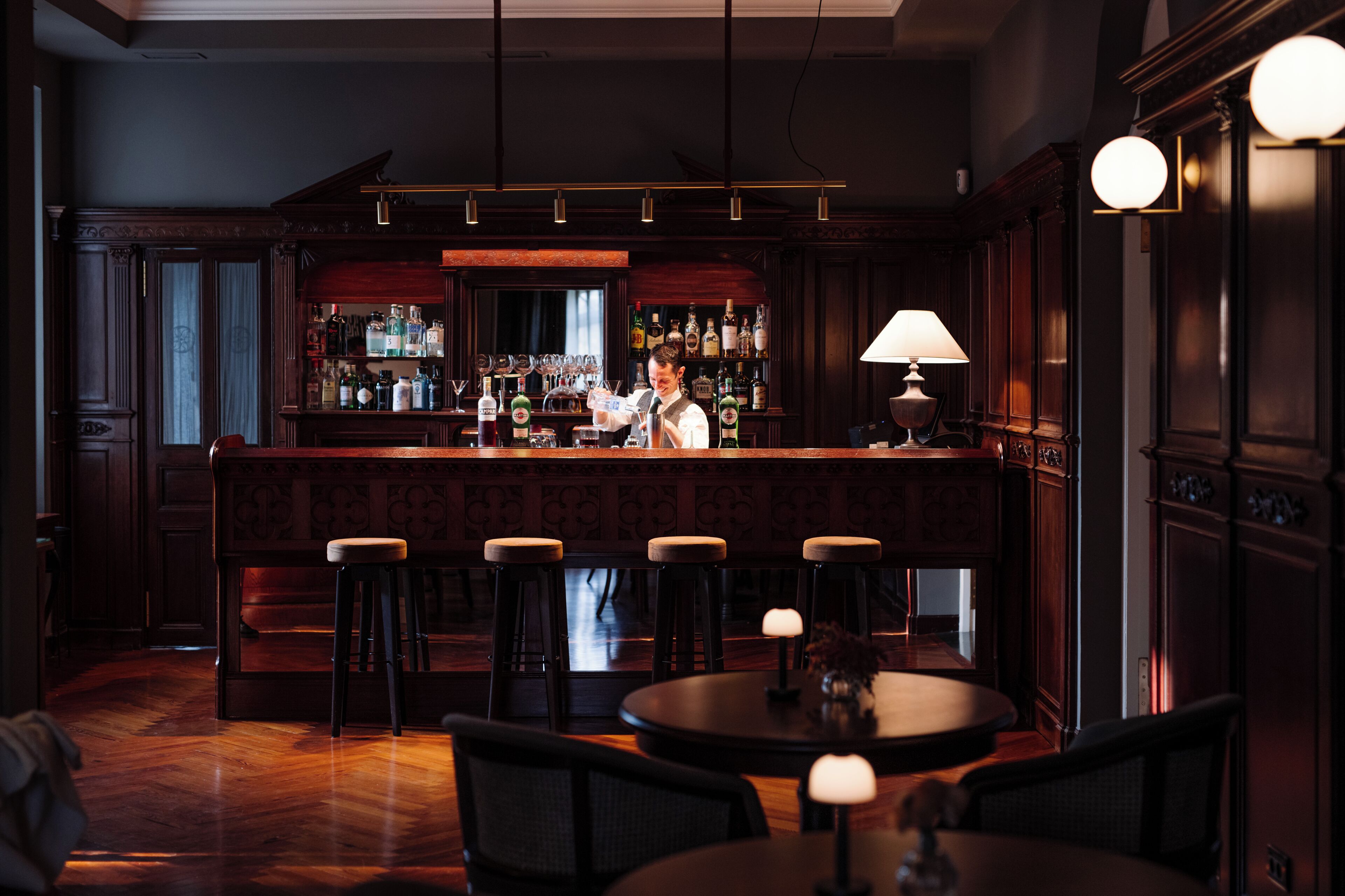 A bar area with stools, a bar counter, and a bartender.