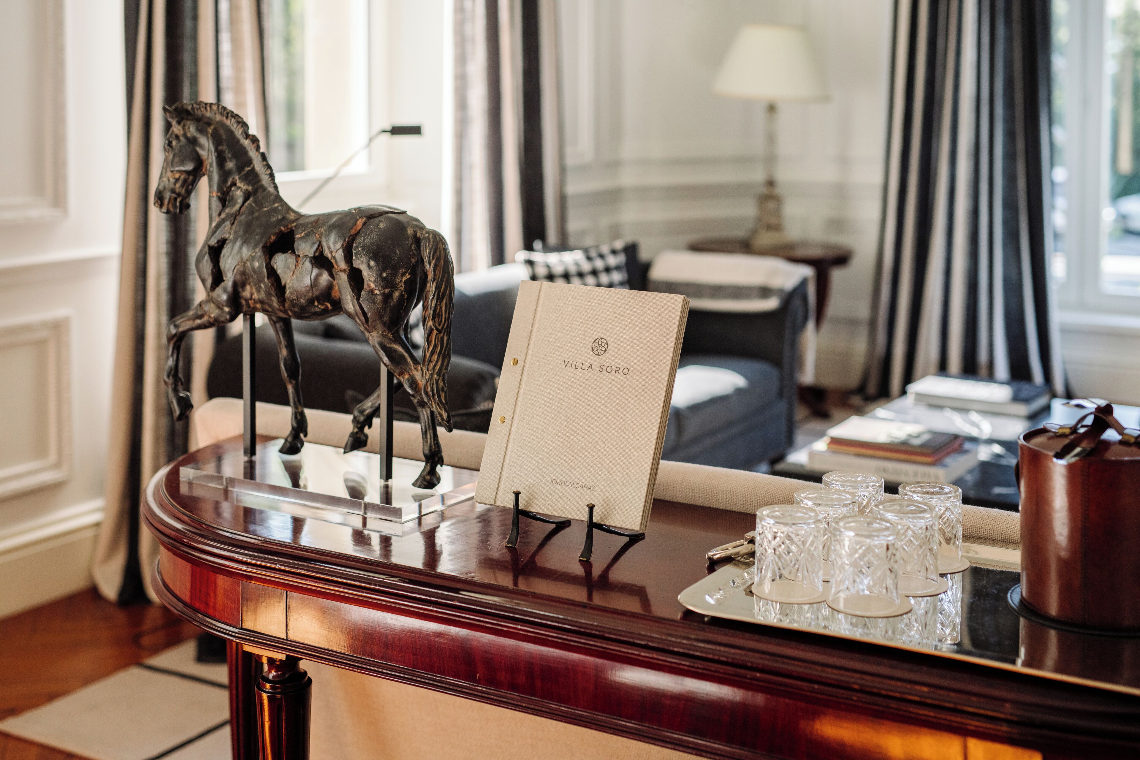 A wooden reception desk with a horse sculpture, a framed document, and a tray with glasses.
