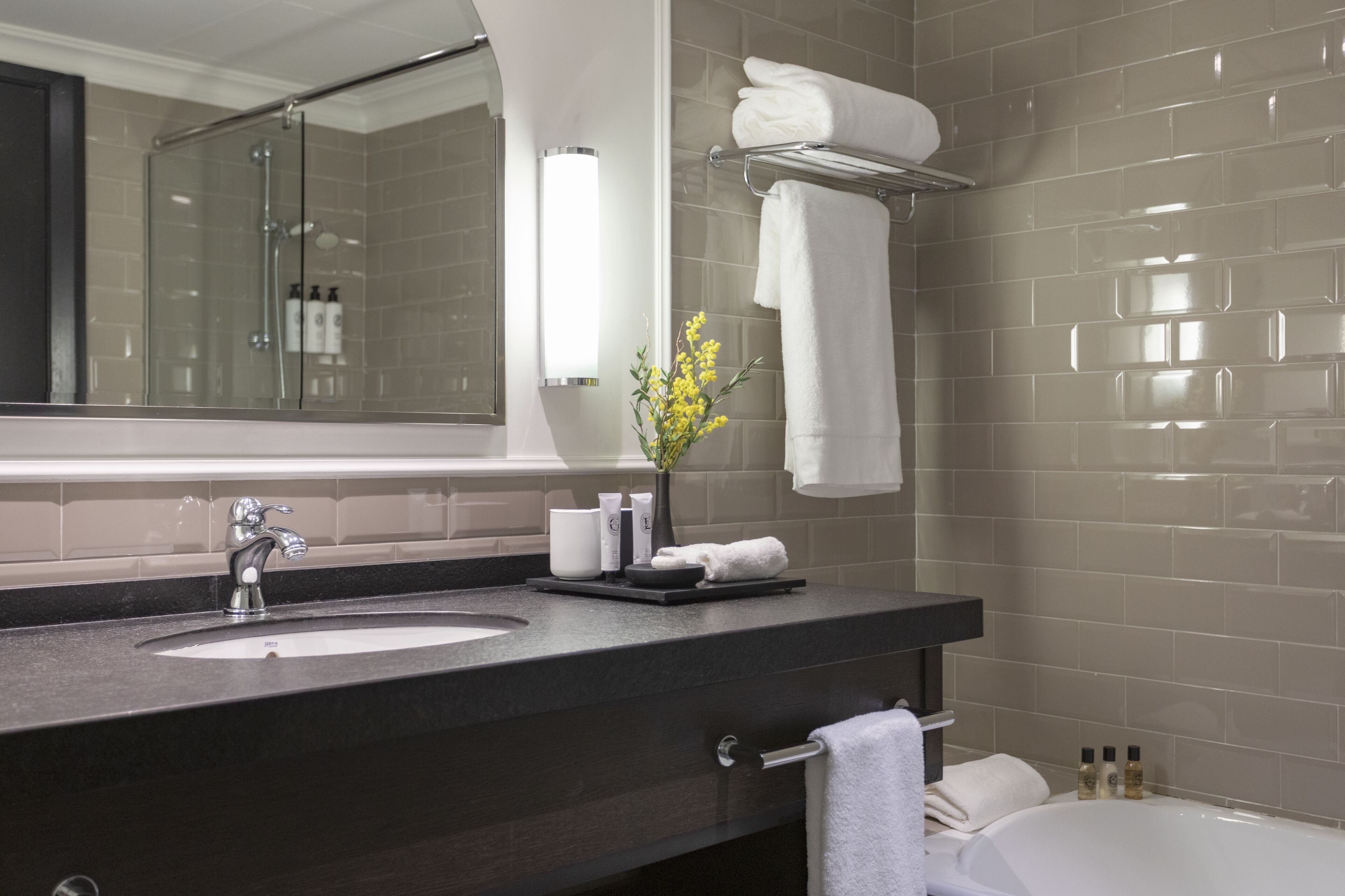 A modern bathroom with a large mirror, a sink, a shower, and a bathtub. There are towels and toiletries on the counter.