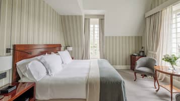 A hotel room with a large bed, a bedside table, a chair, a small table with a vase, and a window with curtains.