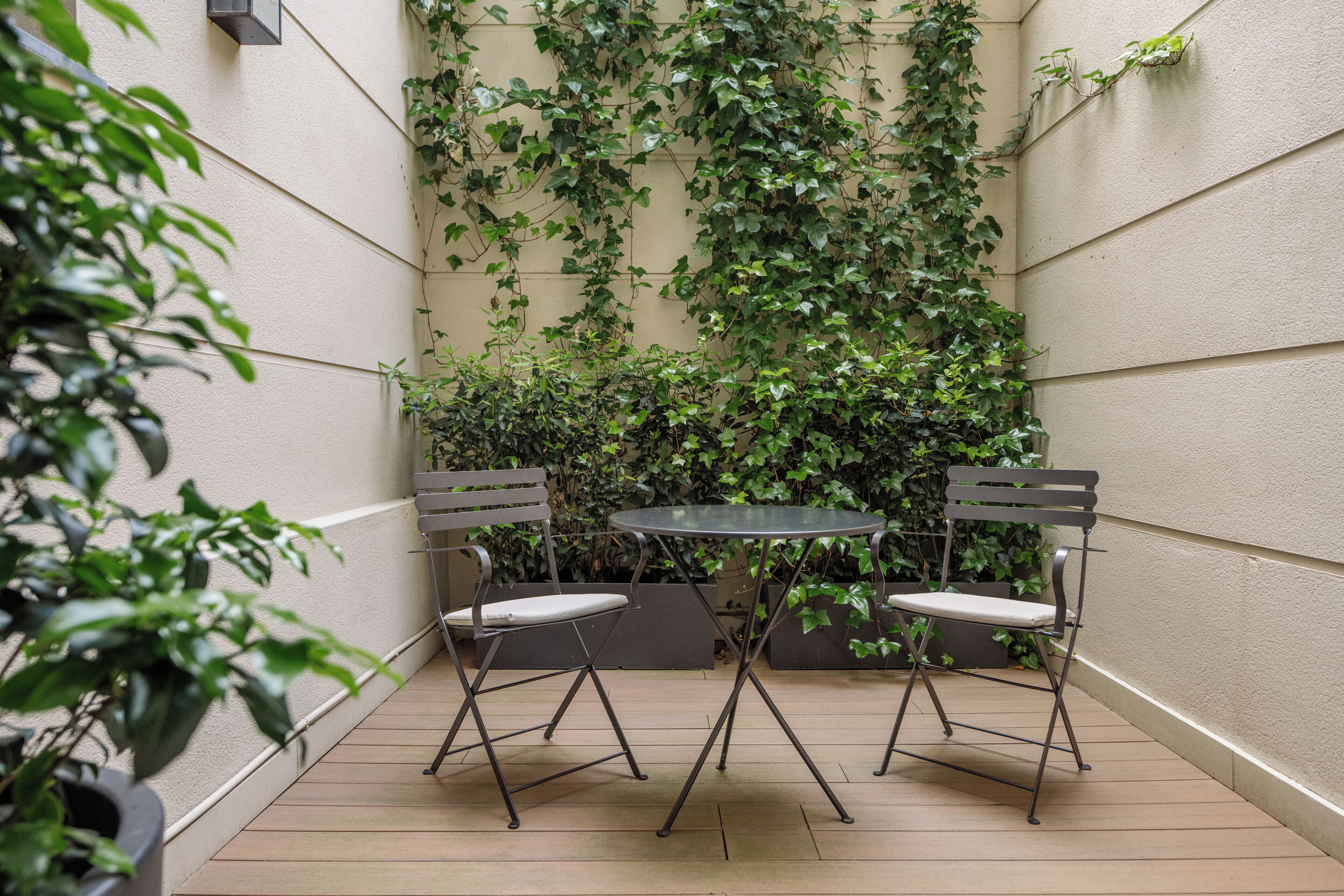 Eine kleine Terrasse mit zwei Metallstühlen und einem Tisch, umgeben von einer mit Grünbecken bewachsenen Mauer.