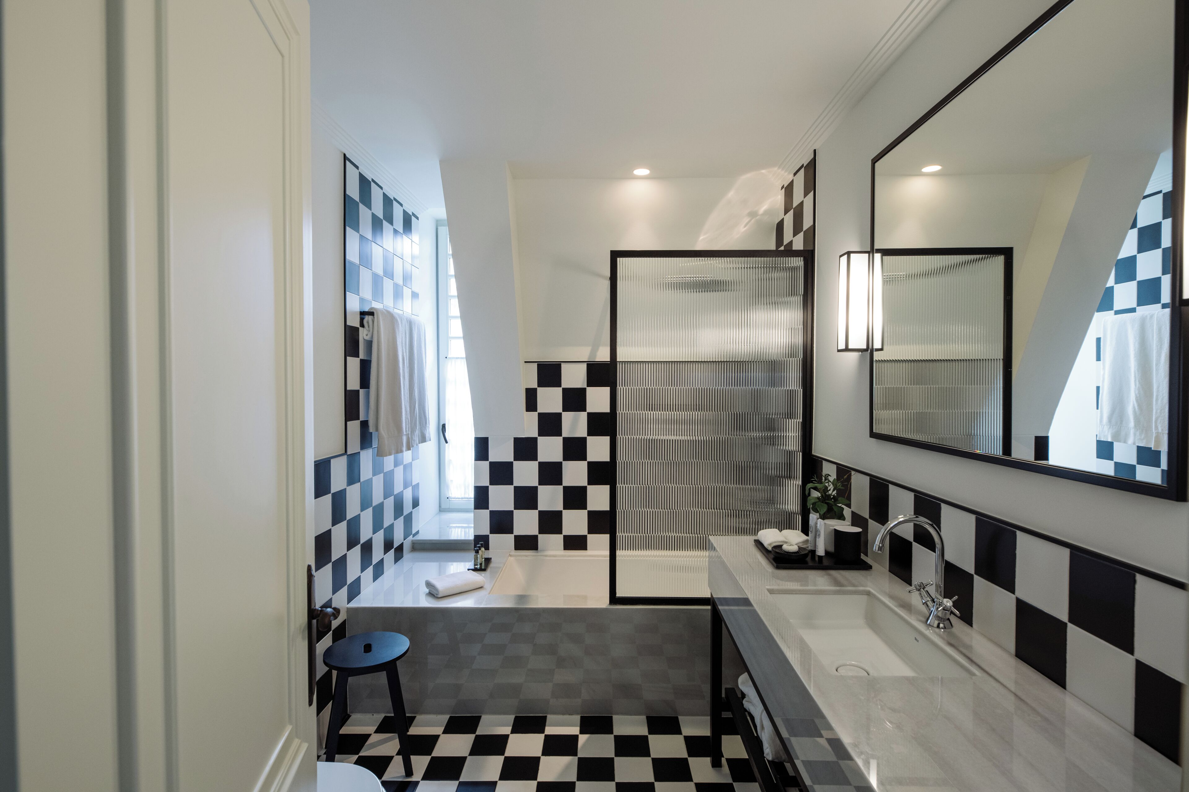 A modern bathroom with a checkered floor, a large mirror, a bathtub, and a sink.
