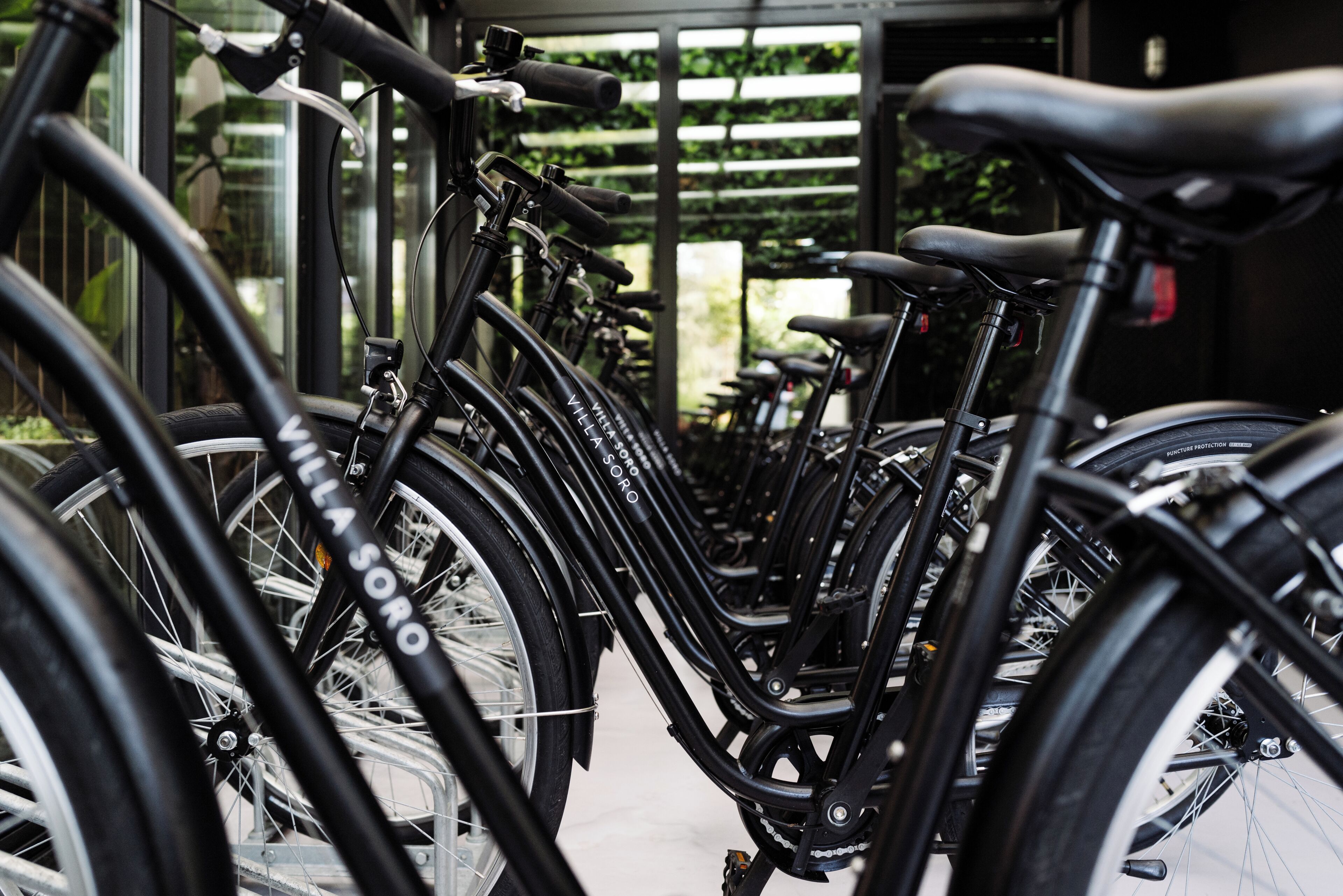 A row of bicycles parked in a covered area with a view of greenery outside.