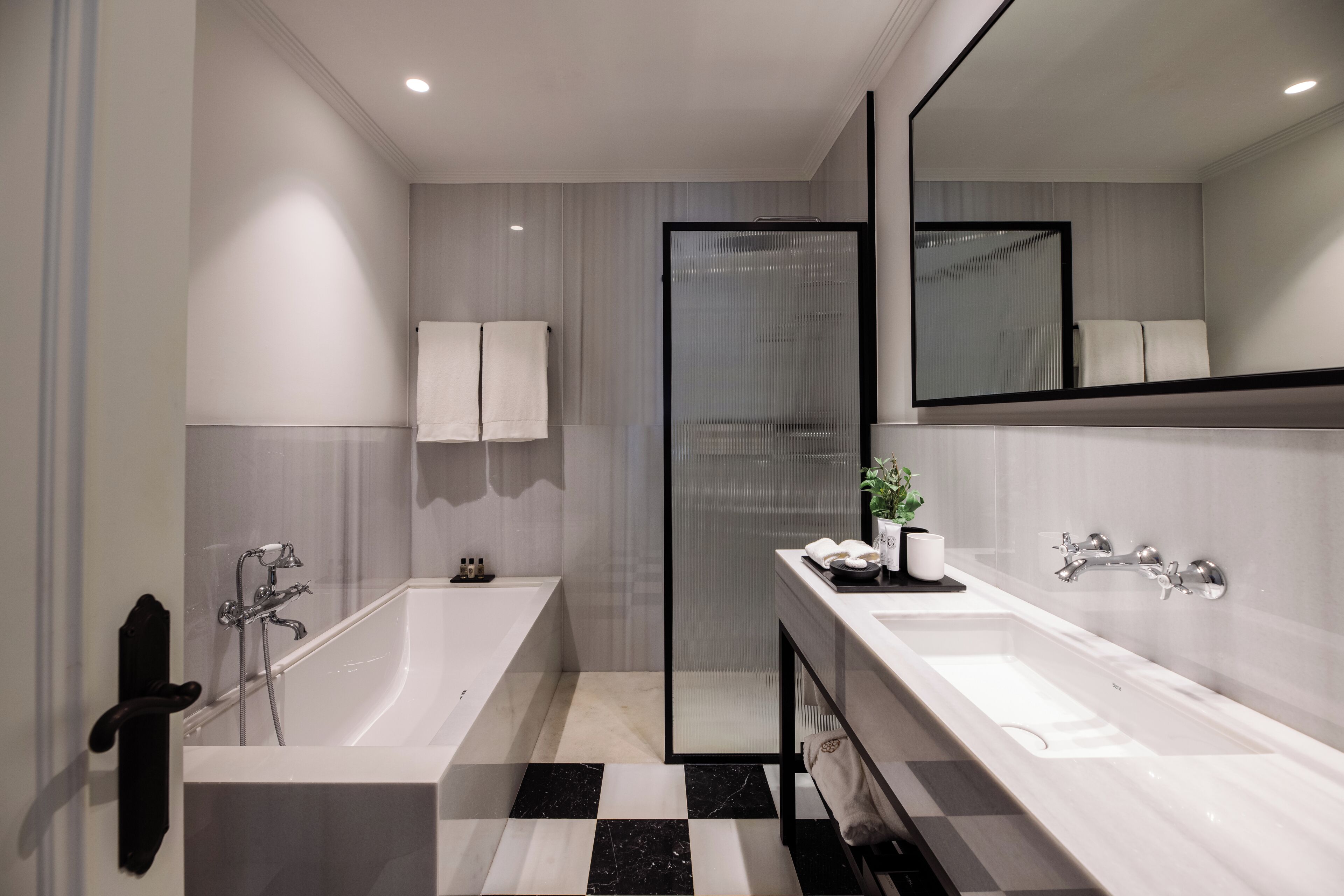 A modern bathroom with a bathtub, a shower, a double sink, and a large mirror.