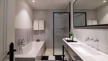 A modern bathroom with a bathtub, a shower, a double sink, and a large mirror.