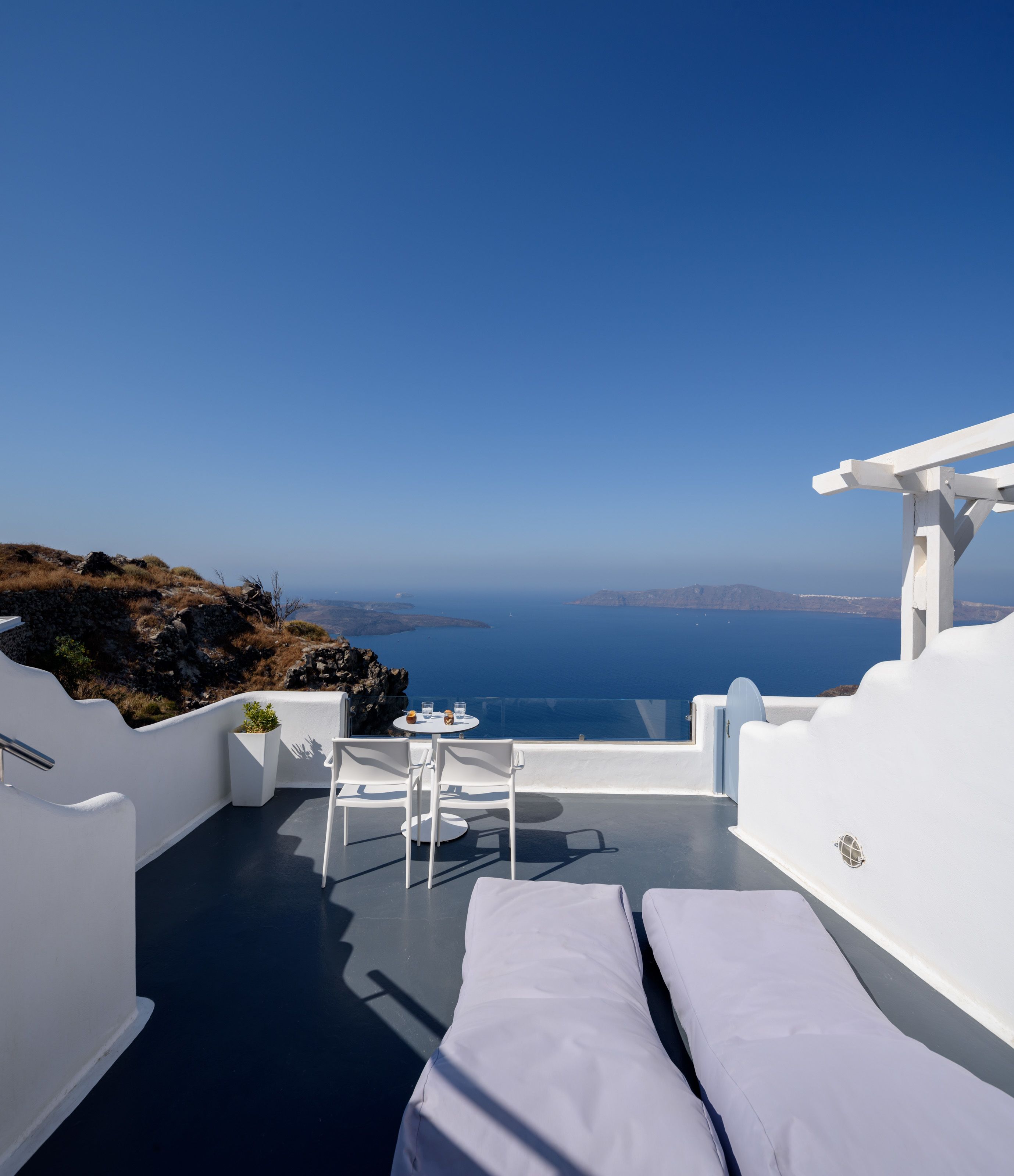 Eine helle Terrasse im Freien mit Tisch und Stühlen, mit Blick auf das klare, blaue Meer und die entfernte Küste.
