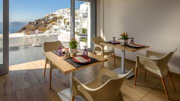 Un comedor moderno con vistas a un pueblo costero, que incluye una mesa de madera, sillas blancas y una planta en maceta.