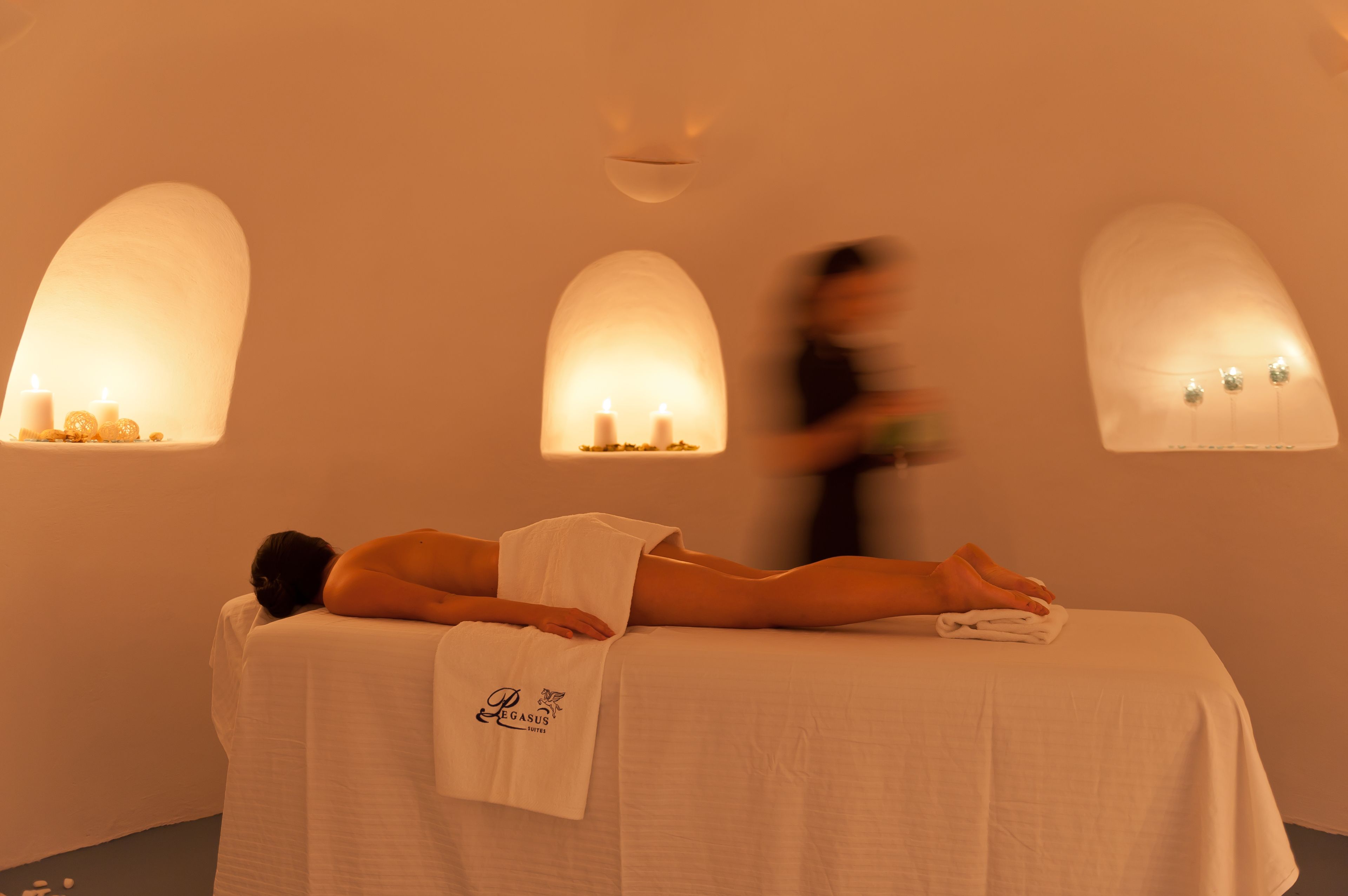 Een massageruimte met een cliënt op een bed, een handdoek over het bed en wandlampen.