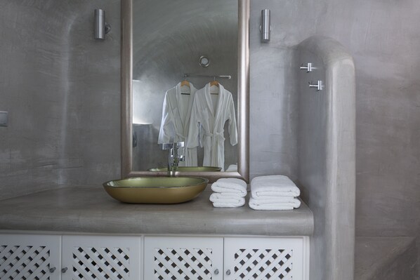 A modern bathroom with a large mirror, a gold sink, and a towel rack with white towels. - Pegasus Spa Hotel (Santorini)