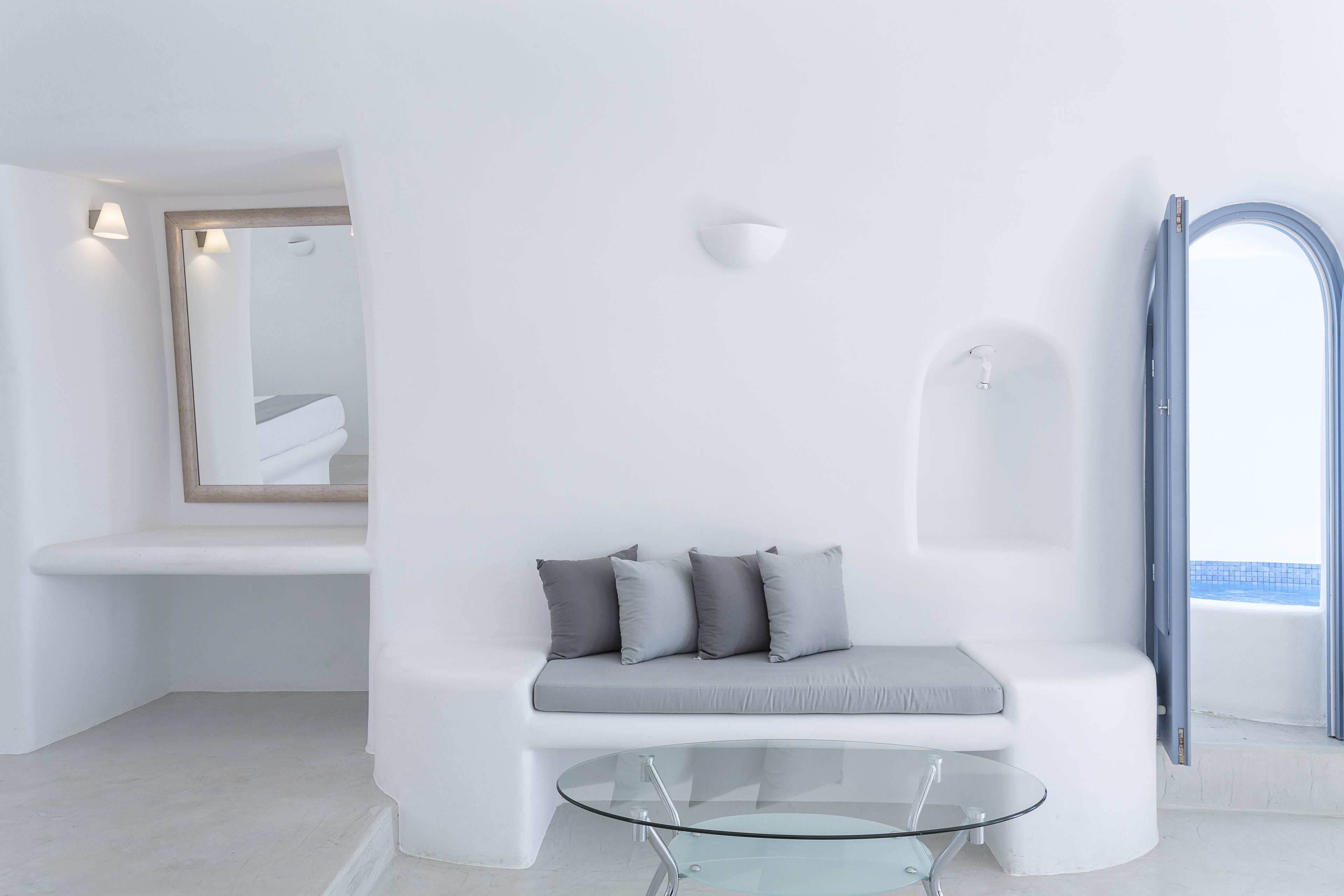 A modern, minimalist room with a white bench, a glass table, and a large mirror.