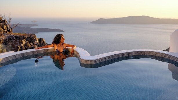 A person relaxing in a infinity pool with a view of the sea and distant islands. - Pegasus Spa Hotel (Santorini)