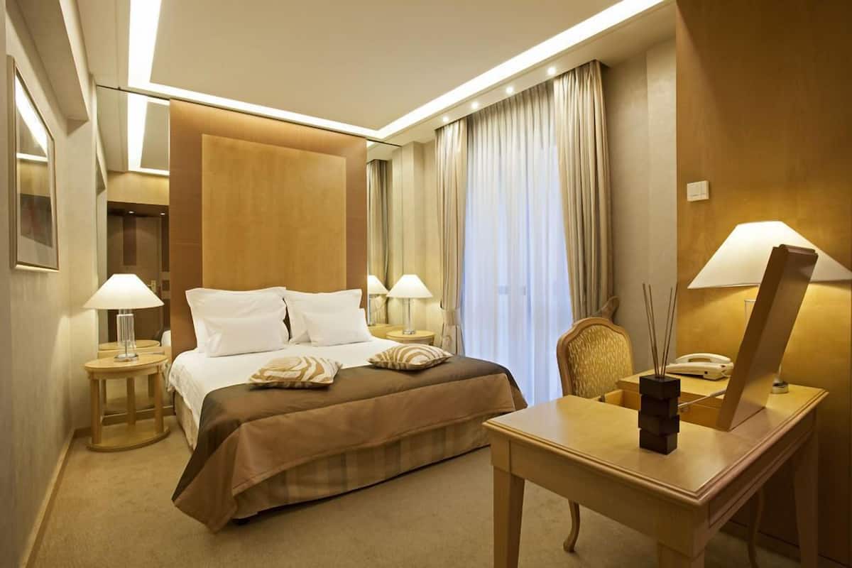 Habitación de hotel con cama, mesitas de noche, escritorio, silla, lámpara, espejo y cortinas.