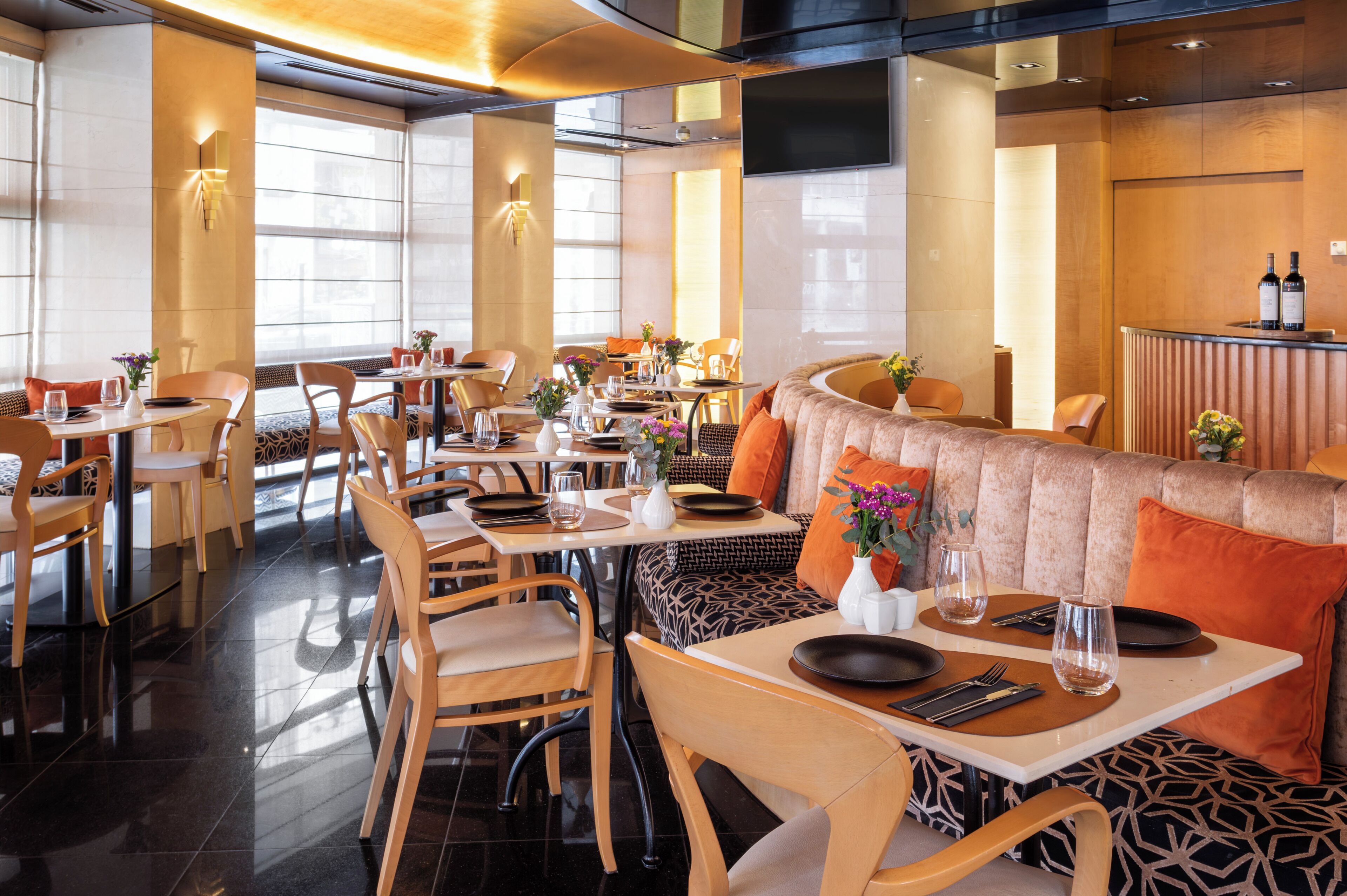 A restaurant with wooden furniture, tables set with plates, glasses, and cutlery, and a counter with bottles.