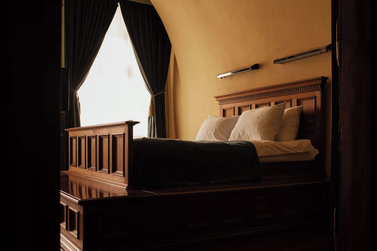 A bed with a wooden headboard, a window with curtains, and a bedside table.
