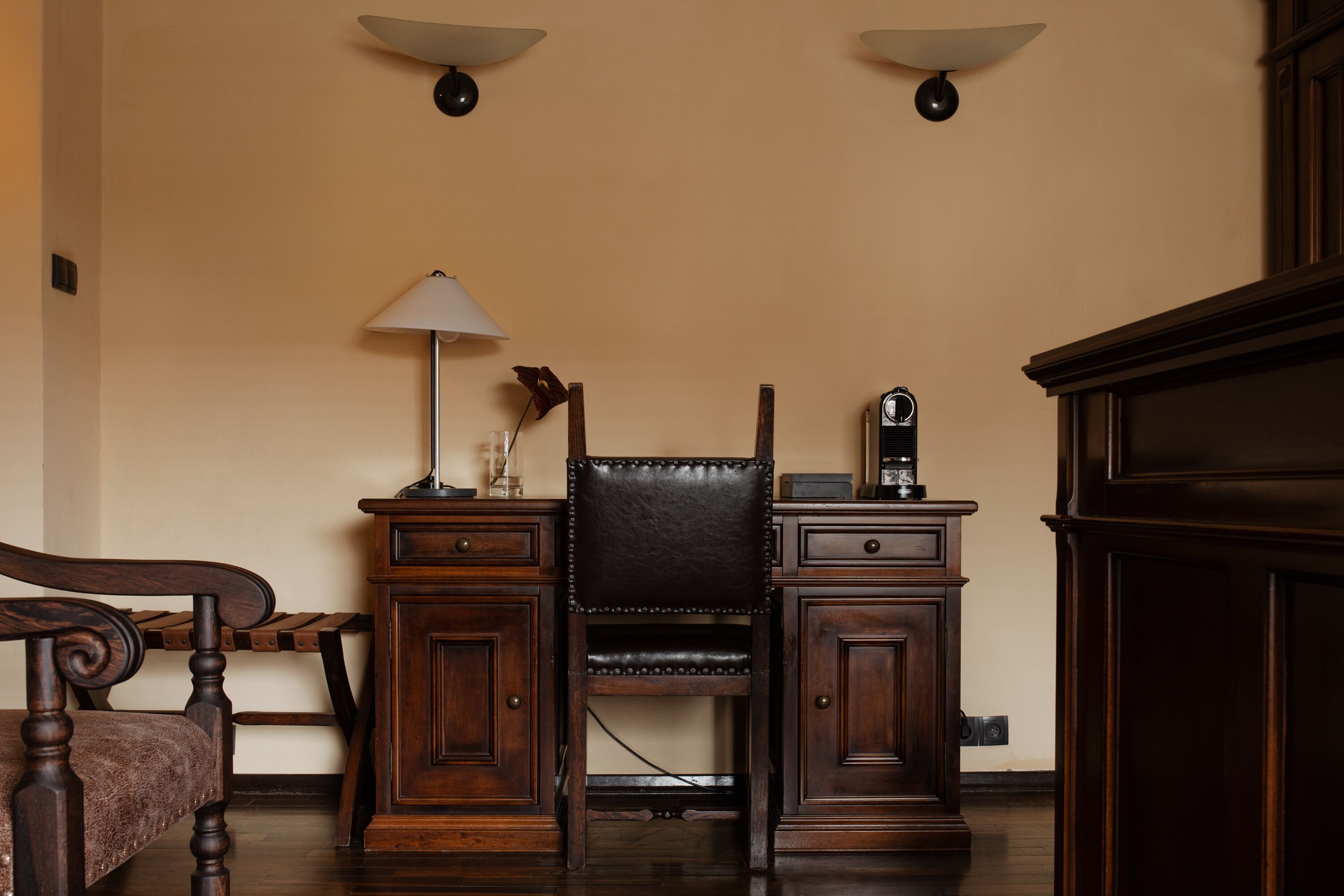 Ein Zimmer mit einem Holzbett, einem Schreibtisch mit Schubladen, einer Lampe und einem Wandradio.