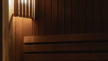 A wooden bench with a slatted backrest and a lower shelf, positioned against a wooden wall with vertical paneling.