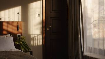 Une chambre à coucher avec un lit, une table de chevet avec une lampe, une porte et une fenêtre avec des rideaux.