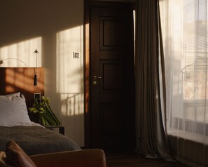 A bedroom with a bed, a bedside table with a lamp, a door, and a window with curtains.