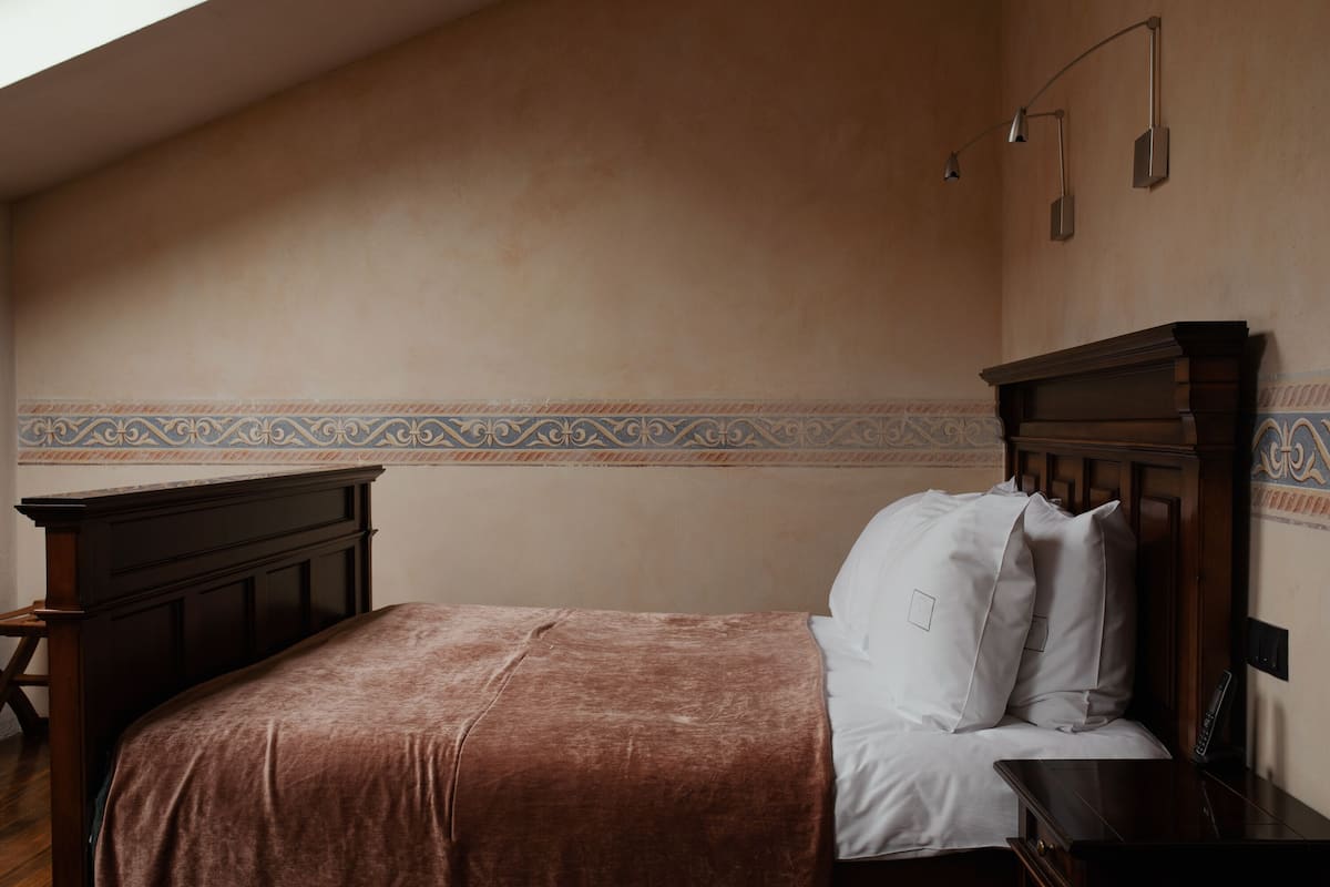 A bedroom with a wooden headboard, a brown bedspread, white pillows, a bedside table, and a nightstand.