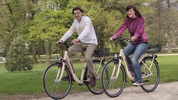 Twee personen fietsen op een pad in een park met bomen en gras.