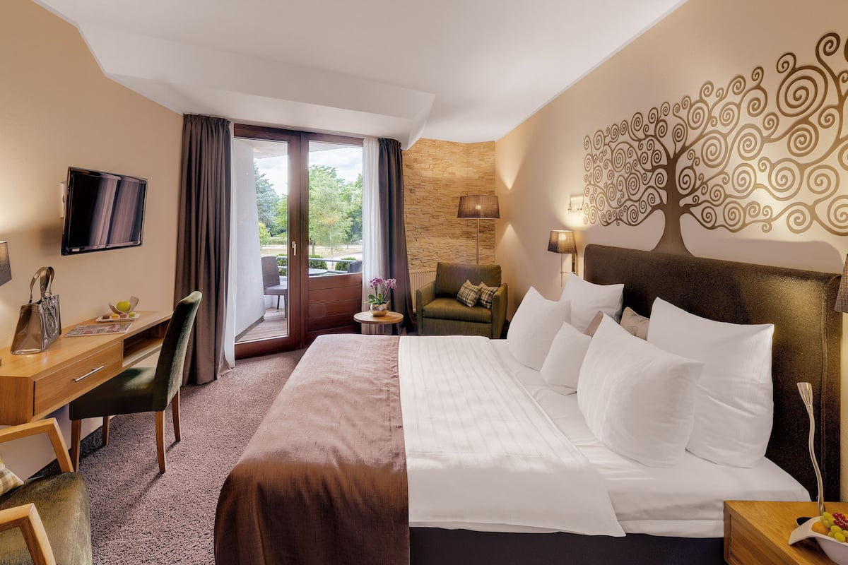 A hotel room with a bed, desk, chair, TV, and a view of the outdoors.