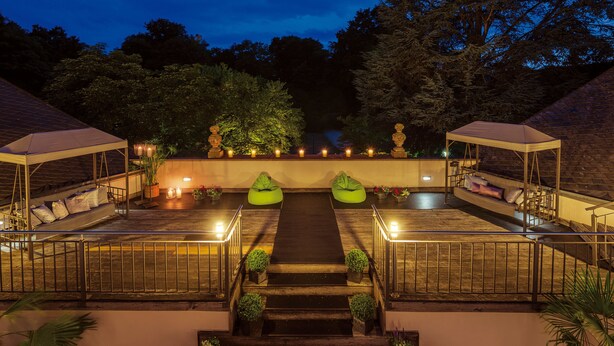 Una terraza en la azotea con zona de estar cubierta por una marquesina, un pequeño jardín y una escalera que conduce al nivel superior.