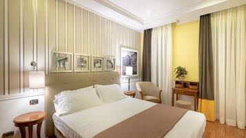 Quarto de hotel com uma cama grande, uma mesa de cabeceira, uma cadeira, uma pequena mesa com uma planta e uma parede com quadros.
